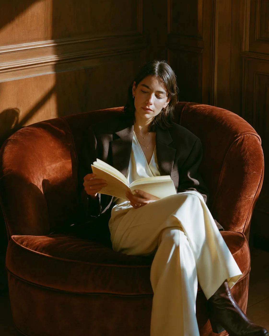A woman reading a book in a sunlit, wood-panelled room