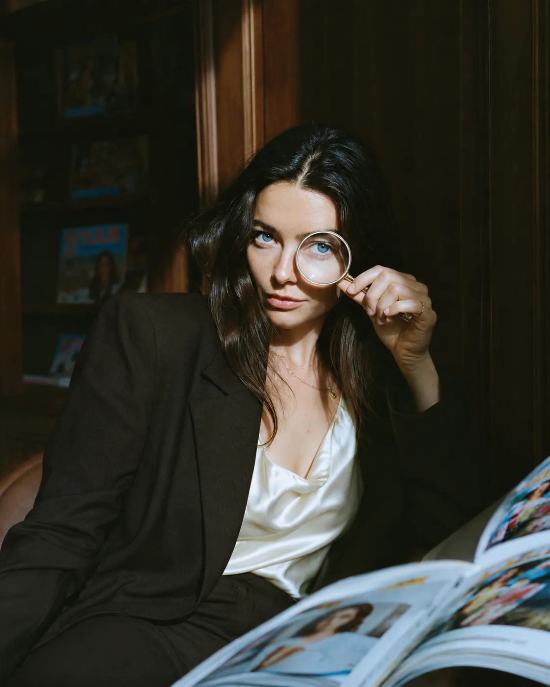 A woman holding a magnifying glass to her eye while reading a magazine