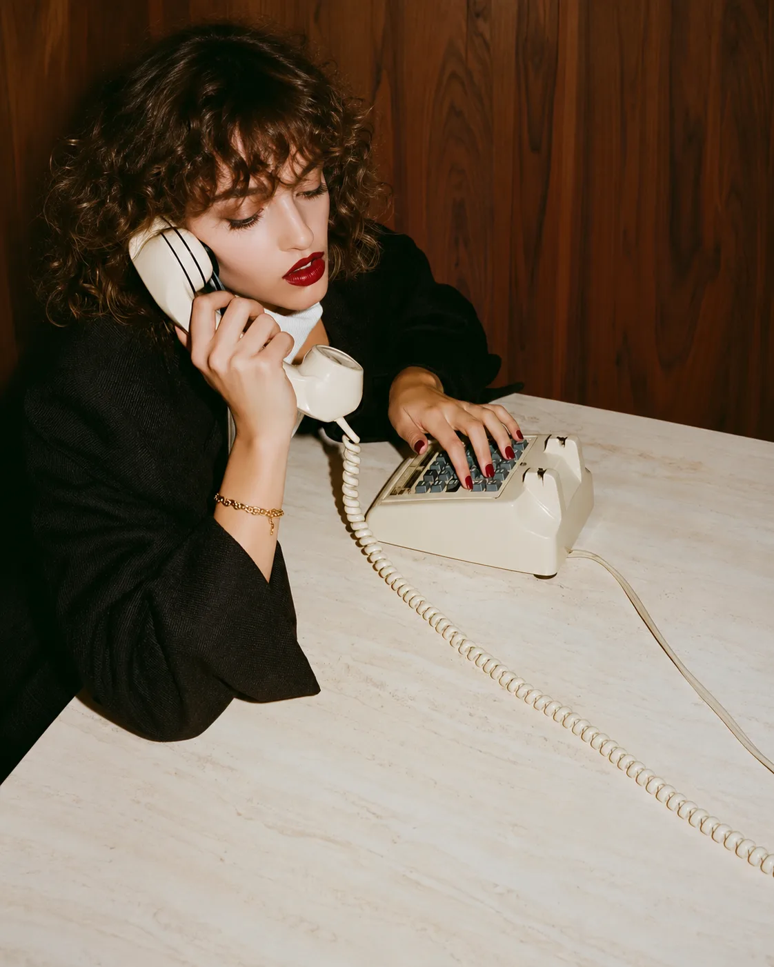 A woman talking on a vintage telephone at a desk